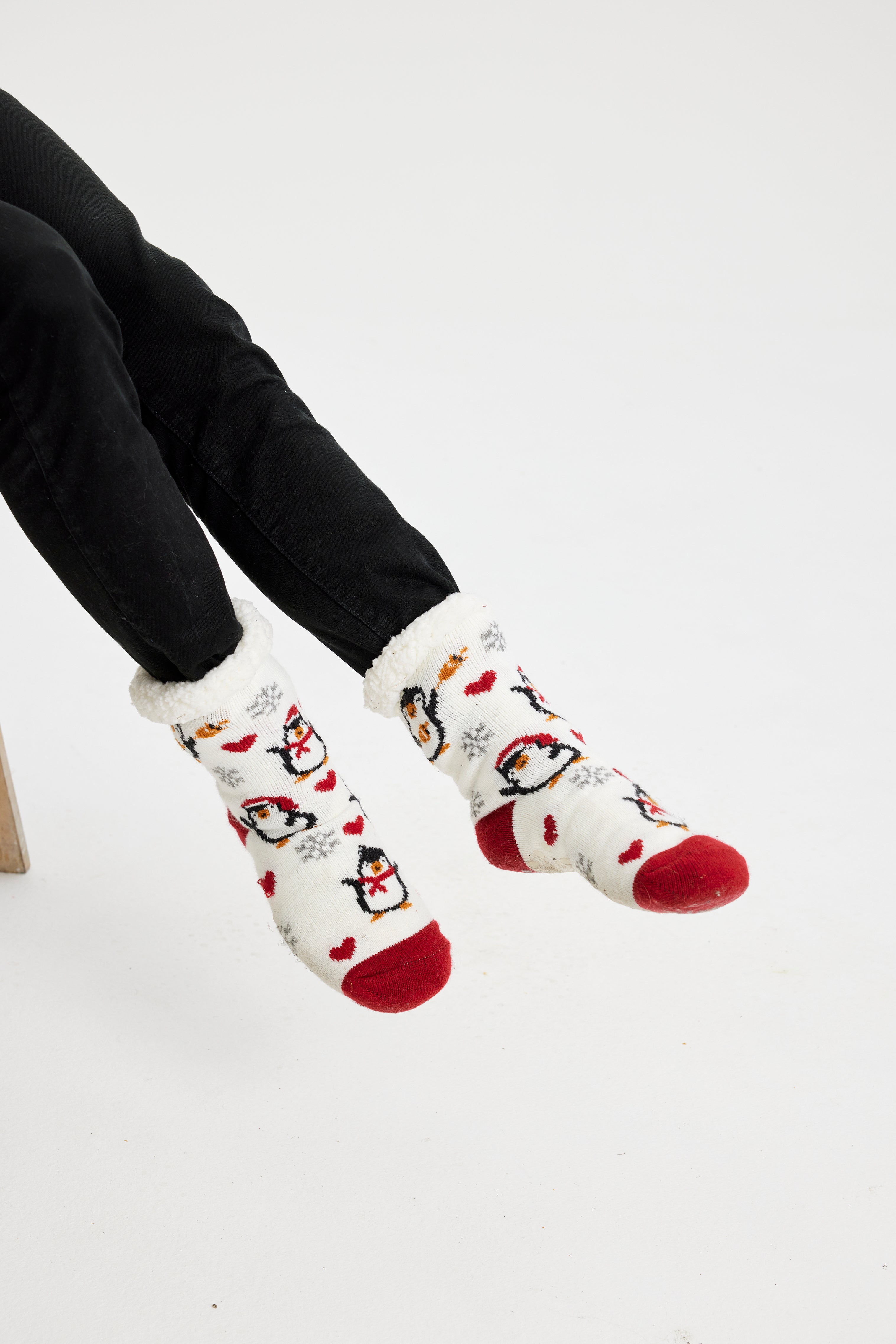 Ein Paar Beine, die ein Paar rote und weiße Weihnachtssocken mit Pinguinen darauf tragen.